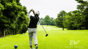 A golfer stands in his follow-through stance and watches his ball after a hit.