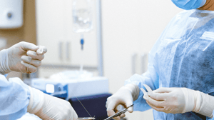 Two people in scrubs sew up an incision