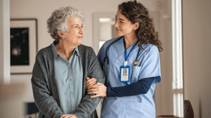 A home health nurse walks arm in arm with an elderly woman.