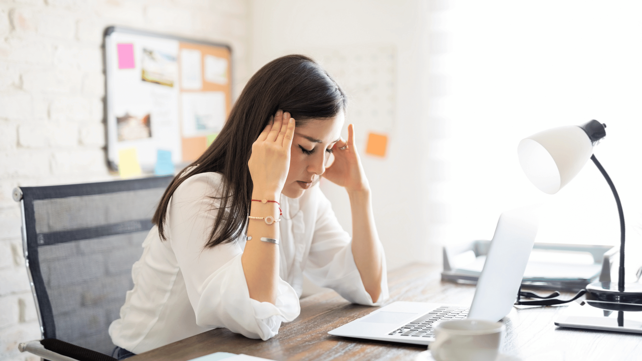 A woman sitting at her desk clutches her head in pain.