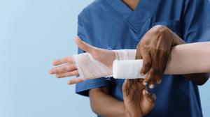 A man in scrubs wraps gauze around a person's wrist.