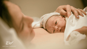 A mom lays in a bed with her newborn baby on her chest.