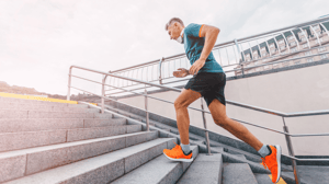A male runner runs up concrete stairs.