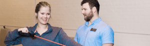 A man watches a woman pull resistance bands. 