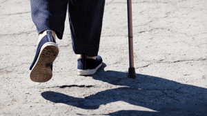 Close-up of a person's feet walking on a concrete sidewalk, holding a cane.