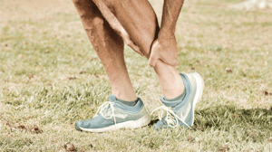 A man bends down to grip his leg.