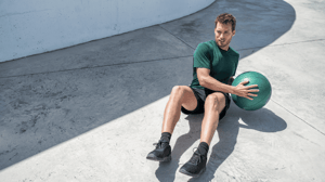 A man sits on the ground doing Russian twists with a medicine ball.