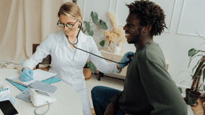 A female doctor listens to a man's heart with a stethoscope.