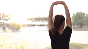 From behind, a woman stretches both arms above her head.
