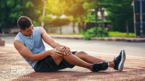 A man sits on the ground, gripping his knee in pain.