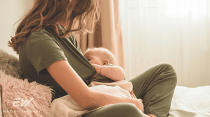 A mom sits on the couch while breastfeeding her baby.