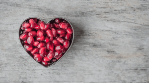 A heart-shaped cup filled with pomegranate seeds. 