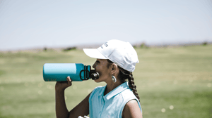 A woman on a golf course drinks from a metal water bottle.
