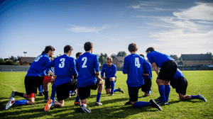 A soccer team kneels in a circle during practice.