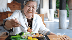 An elderly woman eats outside at a restaurant.