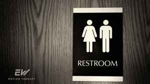 A restroom sign hanging on a dark wooden door.