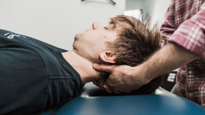 A man lays on a table while getting his neck massaged.