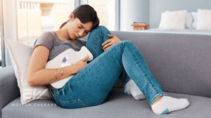 A woman sits on a couch with a hot water bottle.