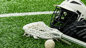 A lacrosse helmet, net, and ball laying on a field.