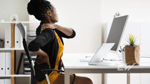 A woman massages her back at her desk.