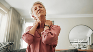 An older woman grabs her neck in pain.