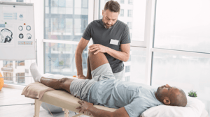 A man bends another man's knee as he lies on a table.