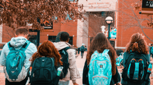 From behind, students walk on a college campus.