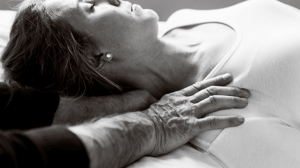 A woman lays on a table while a man massages her neck.