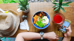 A colorful plate of food in front of a person looking at a watch and phone.