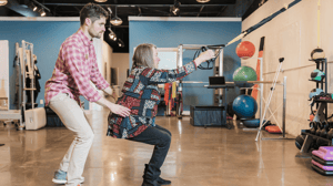 A woman pulls resistance bands while a man guides her from behind.