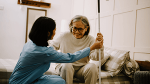 A home health nurse helps an older lady stand up.