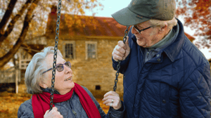 Two older adults sit outside on a swing.