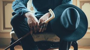 A man sits in a chair holding his cane.