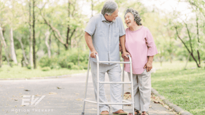 An elderly couple walk along the sidewalk.