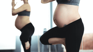 Two pregnant women do a yoga pose.