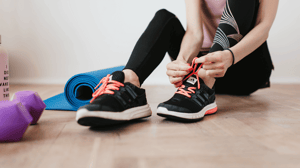 A woman sits on the ground and laces her tennis shoes.