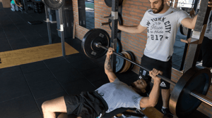 A man watches another man benchpress.