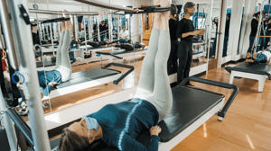 A woman lies on a Pilates reformer with her feet in the air. 