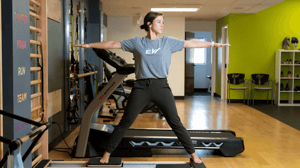 A woman stands on a Pilates reformer. 
