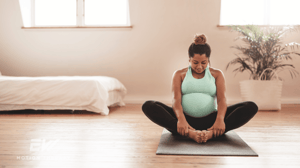 A pregnant woman sits on a yoga mat in a butterfly pose.