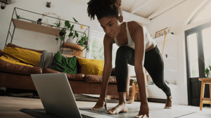 A woman follows a yoga class on her computer at home.