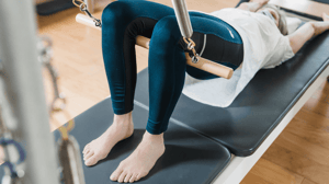 A woman lays on a Pilates reformer with her knees up.