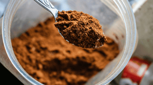 A spoon scooping brown protein powder out of a container