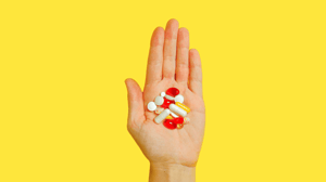 A hand on a yellow background holds various pills.