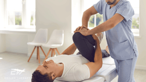 A man lies on a table while a physical therapist works on his knee.