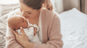 A mom sits on her bed holding her newborn.