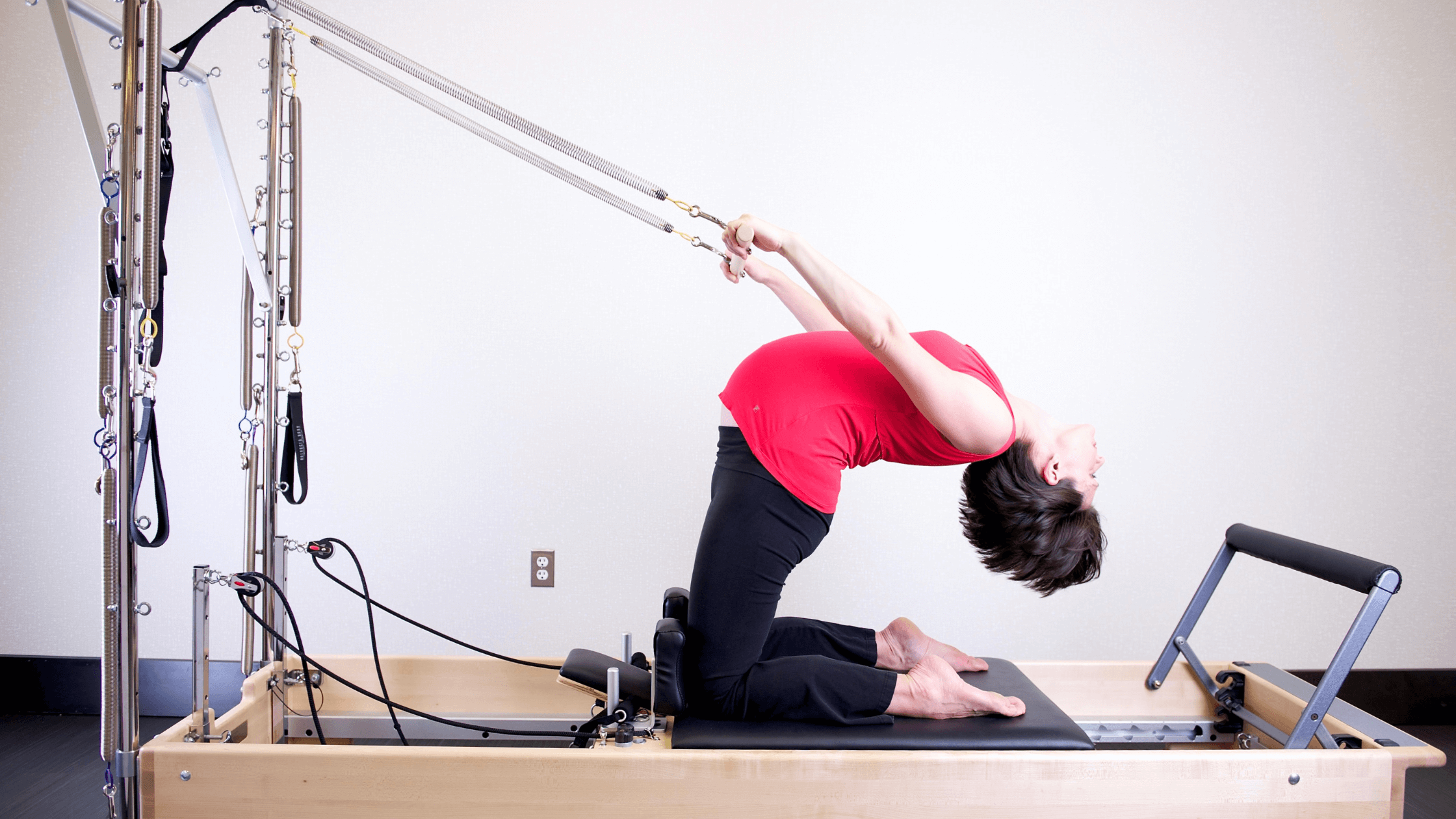 A woman bends backward while kneeling on a reformer.