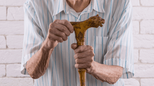 An old man holds the top of a wooden cane.