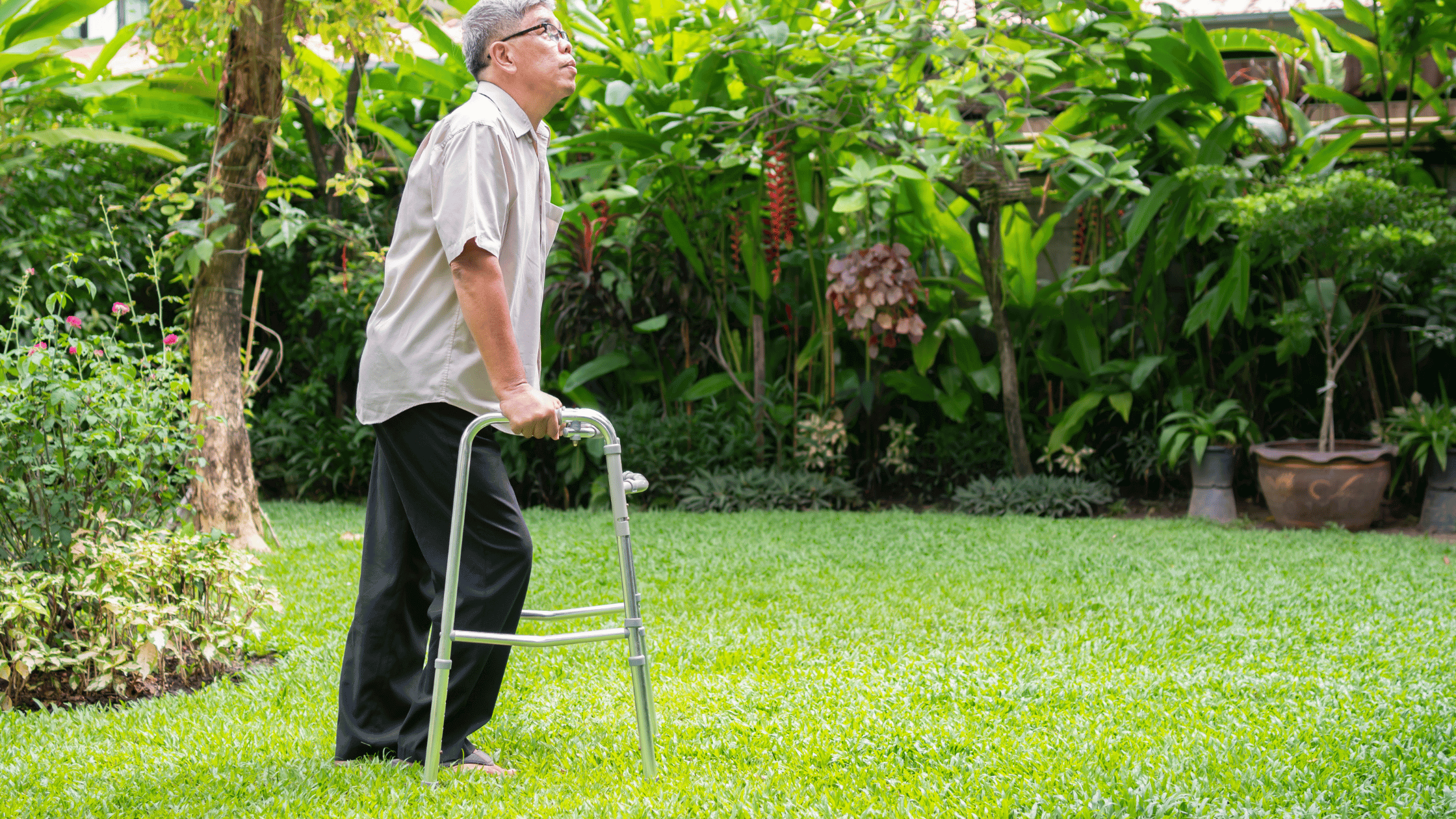 A man stands in his yard, holding on to his walker.