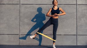 A woman stretches a yellow resistance band between her ankles.